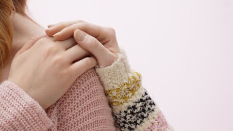 Woman reaching her hand back to her shoulder as another woman's hand is atop her hand in a comforting gesture