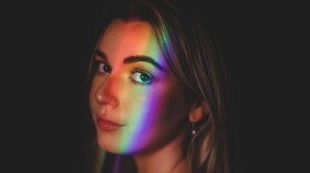 A woman standing in front of a black background with a sliver of light shining on her face.