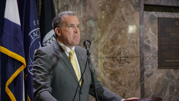 A man in a grey suit with a gold tie stands behind a podium.