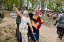 Three people dressed in costumes pose together on a muddy road. The first person is wearing all white and is holding a set of scales and a sword. The second person is wearing a long grey hooded robe and carries a staff. The third person is wearing a red and blue outfit with a gold star structure around her waist. 