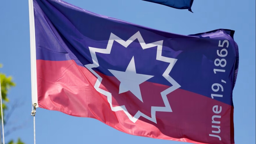 large flag on a flag pole. blue half on top and red half on bottom. there is white star in the middle surrounded by a white sunburst or nova. The letters on one end say June 19, 1865