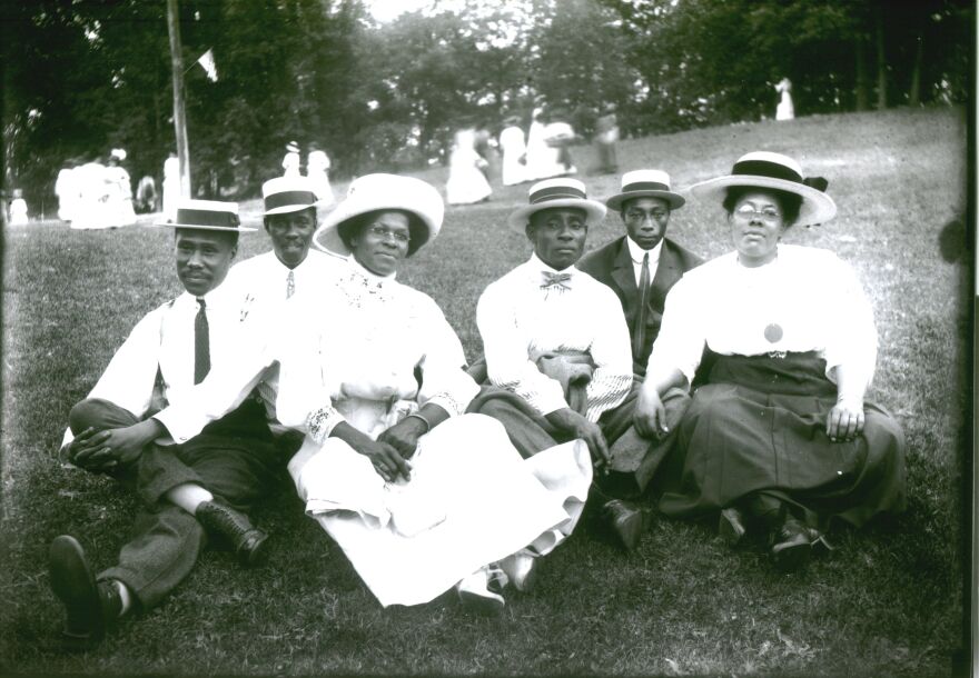 Group of Black men and women sit on a lawn in dandy wear for a portrait.