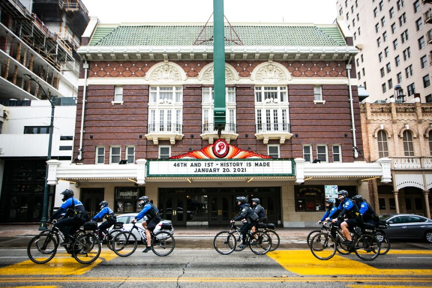 A group of Austin police officers on bicycles rides past the Paramount Theatre, where the marque reads: "46th and 1st – History is made. January 20, 2021.