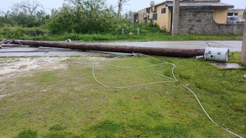 A power pole snapped from its base lies across a road in Rota following the landfall of Typhoon Bavi, with downed lines and a damaged transformer visible amid storm debris.