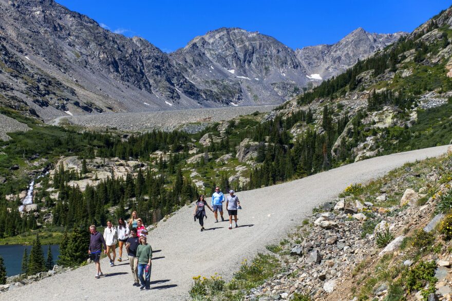 Hikers walk down Blue Lakes Road toward a trailhead near the town of Blue River in Summit County on Friday, Aug. 16, 2024. Tourism in Colorado continues to grow, with a new report from the state’s tourism office showing a 7.3% increase in travelers and a 16.8% increase in spending between 2019 and 2023. In some regions, like the central and northern mountains, growth has slowed. But outdoor leaders still worry about the environmental impacts of long-term trends.