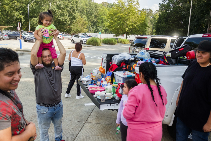 Adults and kids eat lunch in the back up a parked pick up truck.