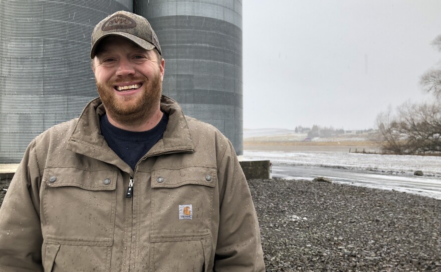 Allen Druffel, 34, of Colton, Wash., stands in front of the co-op silos that hold his unsold chickpeas. Last year he was getting 50 cents a pound for his pulse crop. Now, the going price is 18 cents a pound — well below his cost of production.