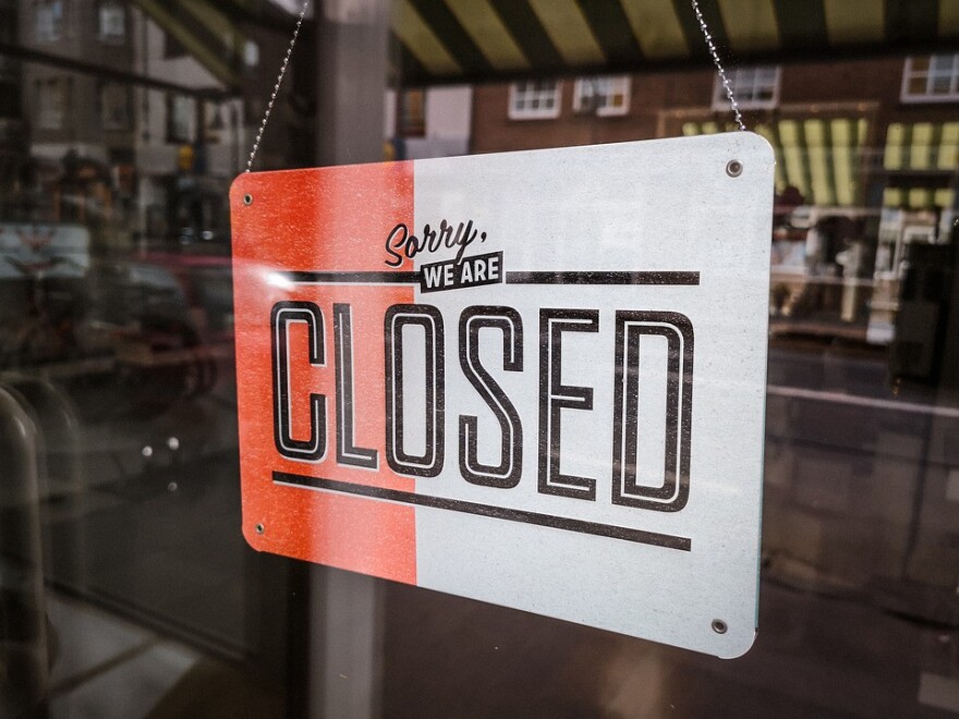 An orange and white closed sign hangs in a store window. 