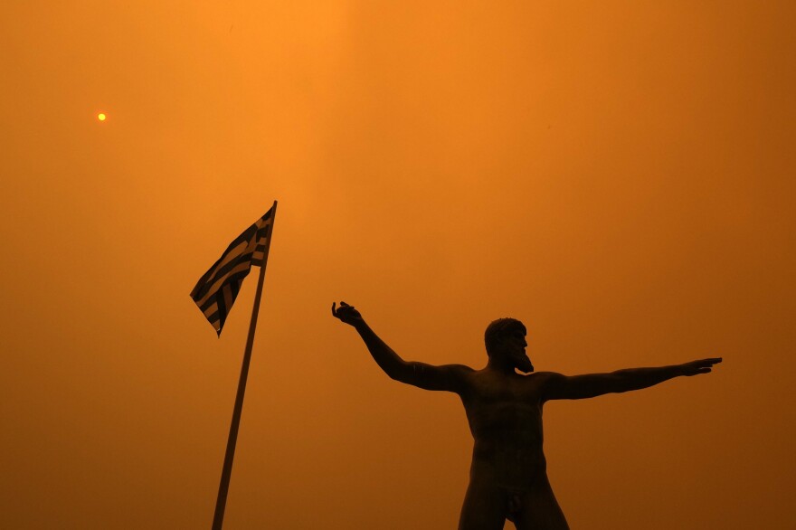 Smoke from wildfire spreads over the statue of Poseidon, ancient Greek God of the sea, at Pefki village on Evia island, about 189 kilometers (118 miles) north of Athens, Greece, Sunday, Aug. 8, 2021. Pillars of billowing smoke and ash are blocking out the sun above Greece's second-largest island as a days-old wildfire devours pristine forests and triggers more evacuation alerts.