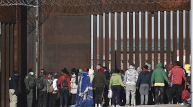 a line of migrants standing at the border of El Paso, Texas