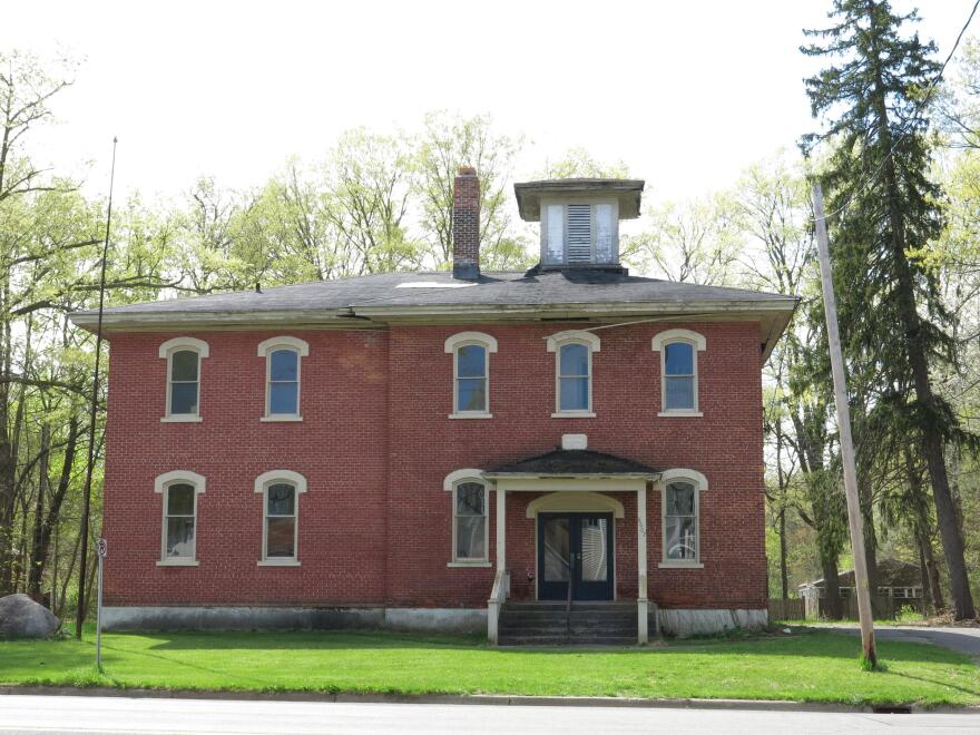 A front view of a two story red-brick building with arched windows and a wooden belfry