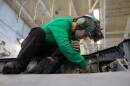 A sailor cleans the wing of an F/A-18F Super Hornet aircraft in the hangar bay of the USS Gerald R. Ford (CVN 78) during Operation Epic Fury.