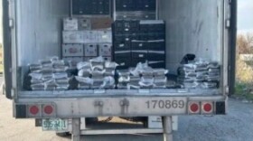 The bed of a semi trailer showing bags filled with cocaine and stacks of boxes