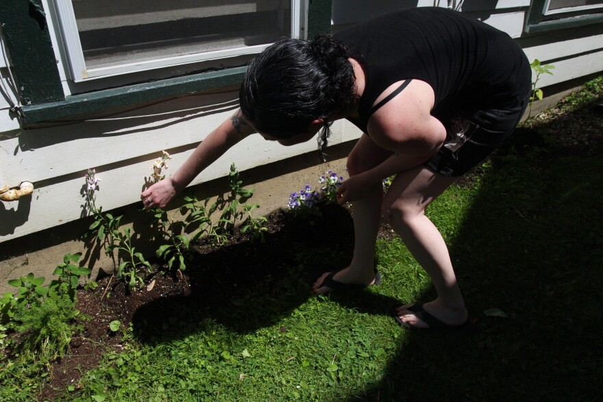 A woman bends down and arranges a flower stalk along the side of a house.