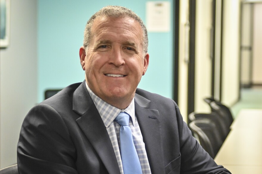 A man is shown, shoulders up looking at the camera and smiling.