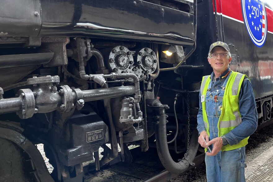 John Watso, a member of the 611 crew, poses next to the locomotive and coal tender decorated in red, white, and blue for America250.