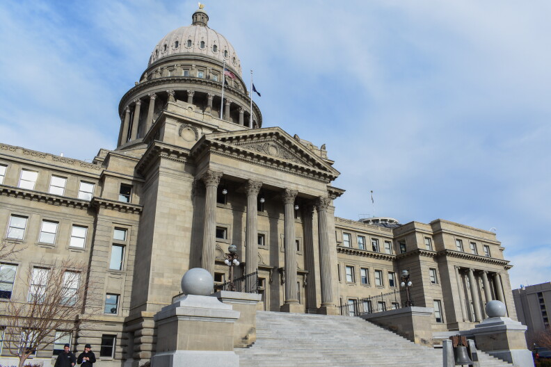 The front of the Idaho Capitol building showing the bell and stairs. Two people are standing on the left-hand side. 