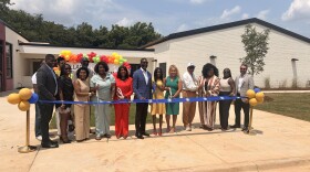 State, local and federal leaders stand behind a blue ribbon, ready to cut it marking the opening of a new early learning center in Birmingham's Titusville community.