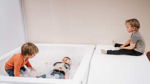 Three children are playing with a white ball pit, filled with clear plastic balls. 