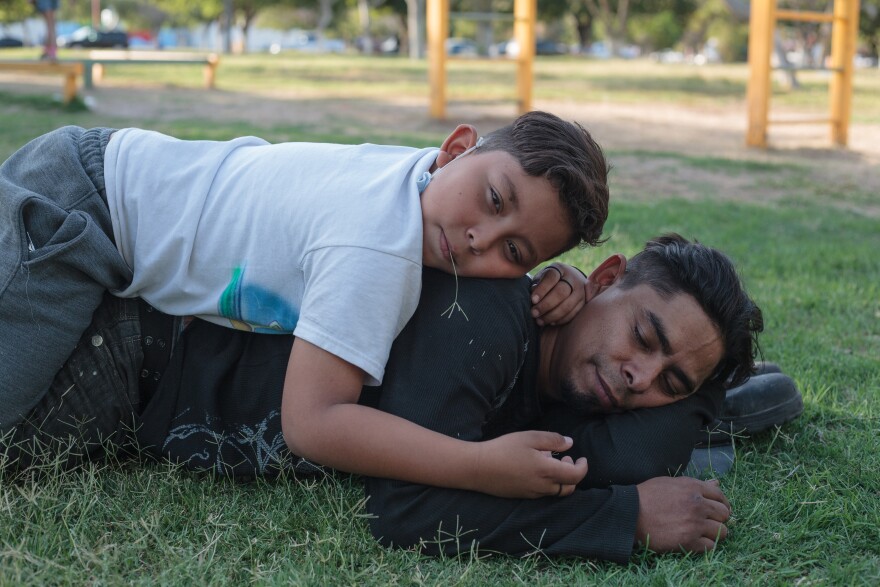 Cesar lays down on the grass with eyes closed while Donovan lays on his back with a piece of straw in his mouth.