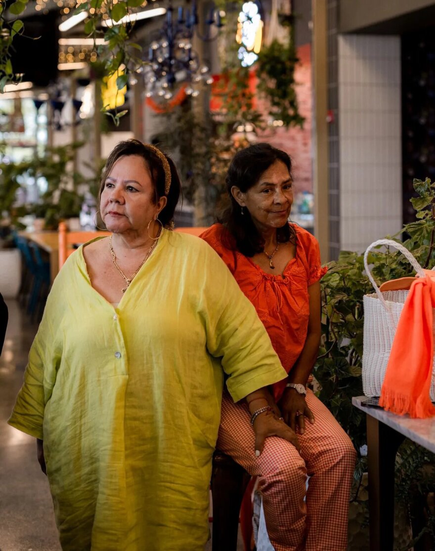 Two women gather together by a table.