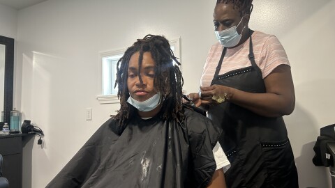 Cornelius Mitchell is sitting in a chair while a hair stylist retwists his deadlocks.