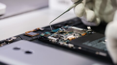 A close up photo of a computer motherboard and tweezers pulling out recyclable mineral materials.