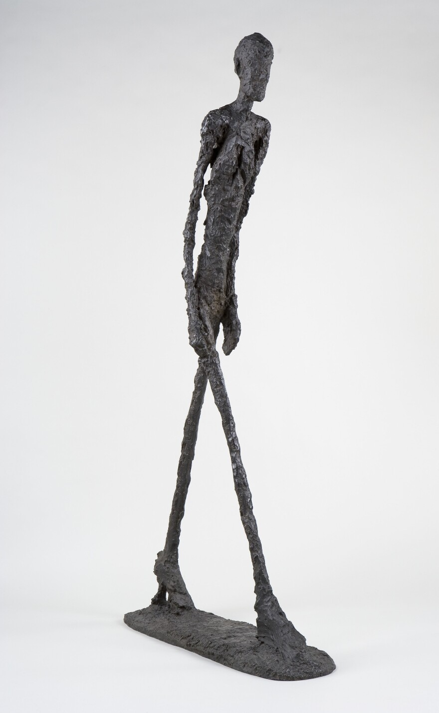 Giacometti's impossibly thin bronze bodies stride like shadows. Above, his 1960 sculpture <em>Walking Man I </em>(<em>Homme qui marche I</em>).