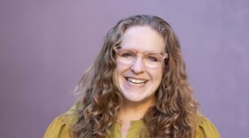 person with long, curly blonde hair. wearing glasess and yellow shirt.