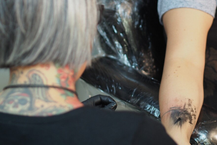 Jacobsen threads an extremely thin needle with cotton thread, dipped in black ink, and passing through the top layer of skin one stitch at a time. The shallow lacerations heal around the ink, becoming darker as they rise further to the surface of the skin. (Photo: Zachariah Hughes, KSKA)