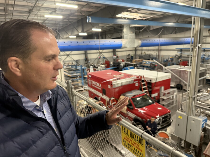 A man in a down jacket stands on a balcony overlooking the shop floor of an emergency vehicle manufacturing facility.