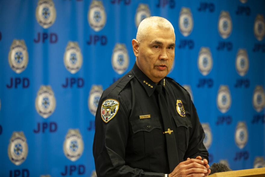 A white, white-haired man in a police uniform speaks at a lecctern in front of blue background