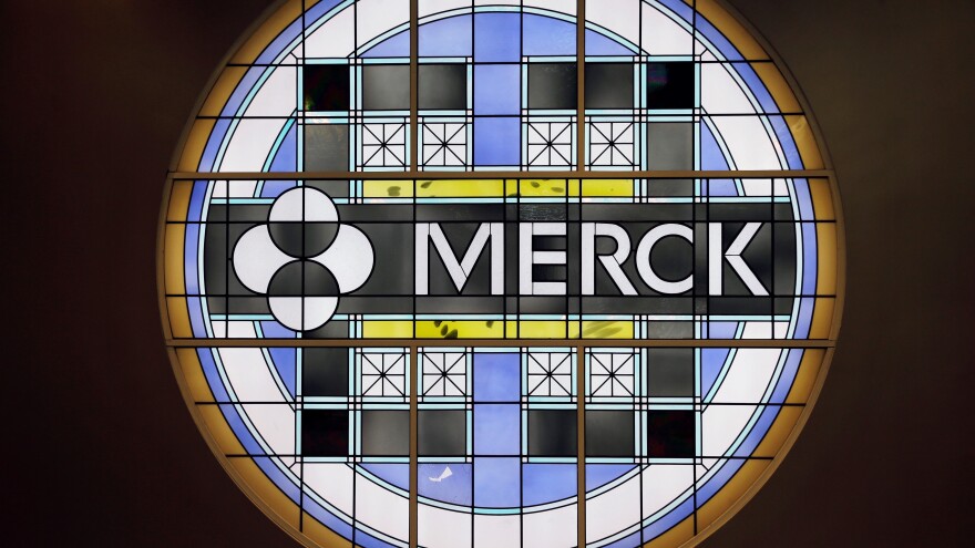 The Merck logo is on a stained glass panel illuminated from behind against a black background. 