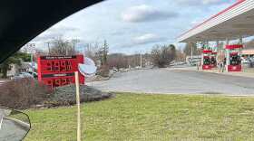 sign at gas station showing gas at three dollars, ninety-nine cents a gallon, with gas pumps in background