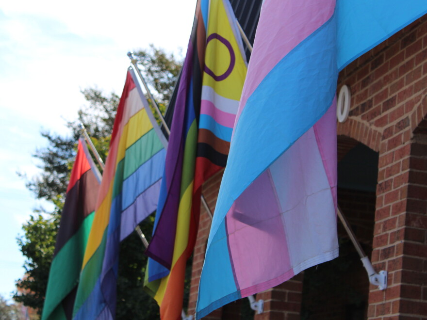 Pride flags on poles from outside wall of brick building 
