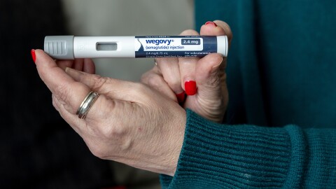 A close up of a woman's hands holding a small tube of Wegovy, an injectable weight loss medication.