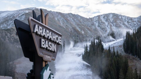 The Arapahoe Basin Ski Area sign in front of a mountain that's beginning to be covered in snow.