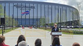 Empire State Development CEO Hope Knight stands at a lectern, with Highmark Stadium looming in the background, describing the importance of minority and women-owned businesses for the stadium's completion.