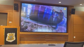 Photo of a room with a large screen where the body cam footage shows an officer with a gun raised