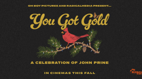 In gold letters it reads "Oh Boy Pictures and RadicalMedia Present... You Got Gold a celebration of John Prine". There is an image of a cardinal sitting on a branch of a pine tree with Christmas lights wrapped around the branch. 