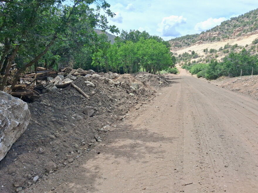 A dirt section of Lone Dome Road beside piles of rocks, sediment and woody debris cleared from the roadway after post-fire runoff.