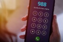 a hand holds a cellphone that is dialing 988