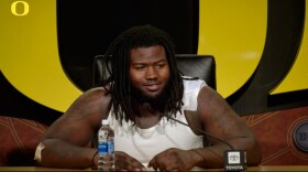 A man sits at a table in front of a microphone at a press conference