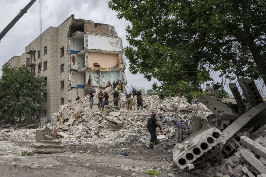 Rescue workers stand on the rubble at the scene of a missile strike that hit a residential apartment block in Chasiv Yar, which is located in Ukraine's Donetsk region. The strike took place Saturday night and left at least 15 people dead.