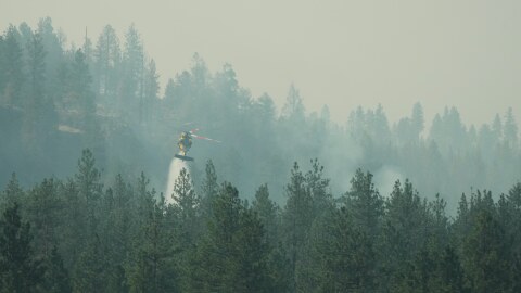 A firefighting helicopter dumps water on a wildfire in the northwest part of Spokane, Wash., Tuesday, Aug. 4, 2026. (AP Photo/Lindsey Wasson)