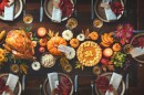 Thanksgiving celebration traditional dinner. Roasted turkey garnished with cranberries on a rustic style table decorated with pumpkins, vegetables, pie, flowers and candles.