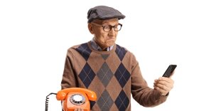 Elderly man holding an old vintage rotary phone and a smartphone.
