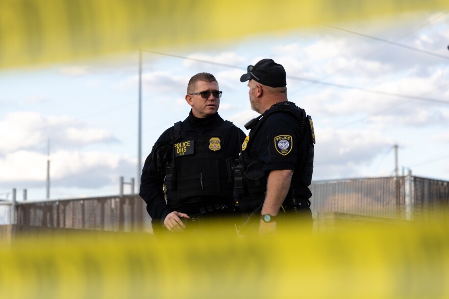 Two federal officers stand outside the Cedar Rapids ICE Field Office during a rally on Tuesday, Sept. 2, 2025, in Cedar Rapids, Iowa. Yellow-and-black police tape can be seen both above and below due to the angle of the photo.