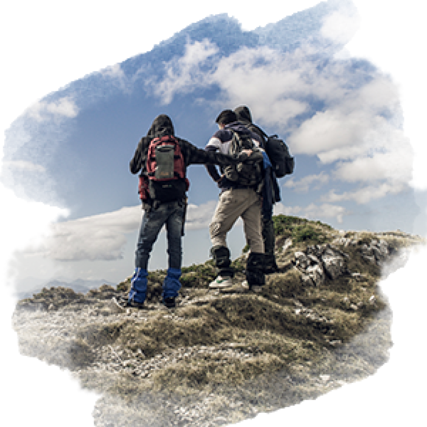 Three people are standing on a mountain together. They are looking away from the camera and toward the distance.