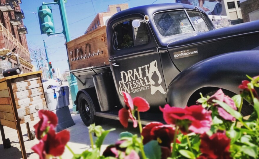 A vintage truck with tap lines installed on the side is parked on the street with plants in the foreground.